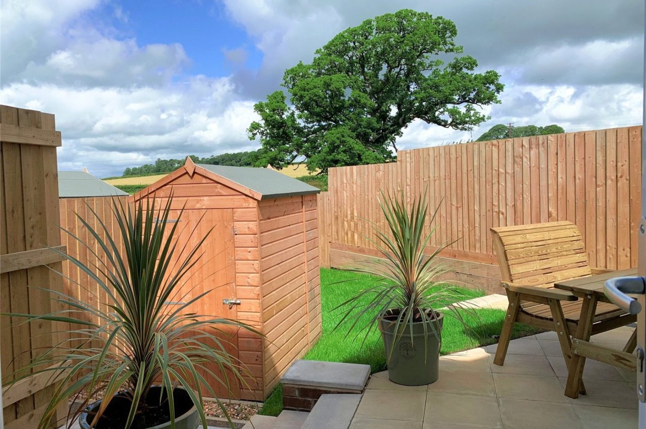 Picture of a garden space, with patio, turf, shed and some planters.