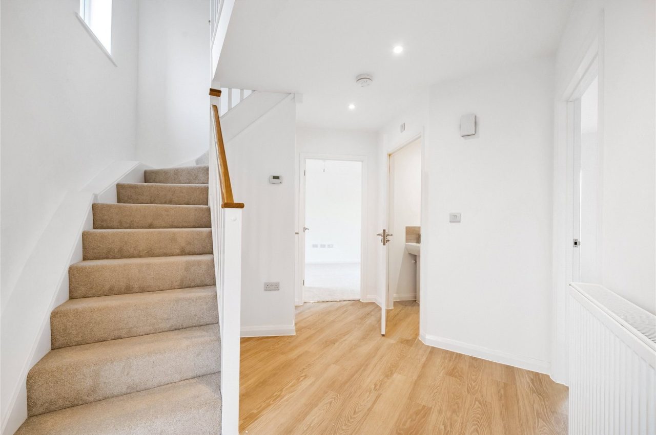 Image of an open hallway, with carpeted stairs leading to the upper floor and doorways through to the lounge and the cloakroom.