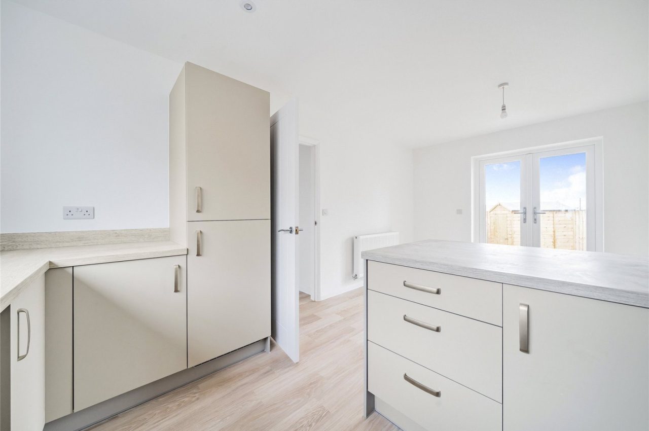 Kitchen dining space, with light grey units, light wood worktop and oak colour floor. To the far end of the image are patio doors with a glimpse of the rear garden.