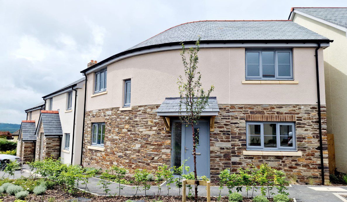 Photo of curved detached house with render and stone finishes, surrounding by a pathway and small plants.