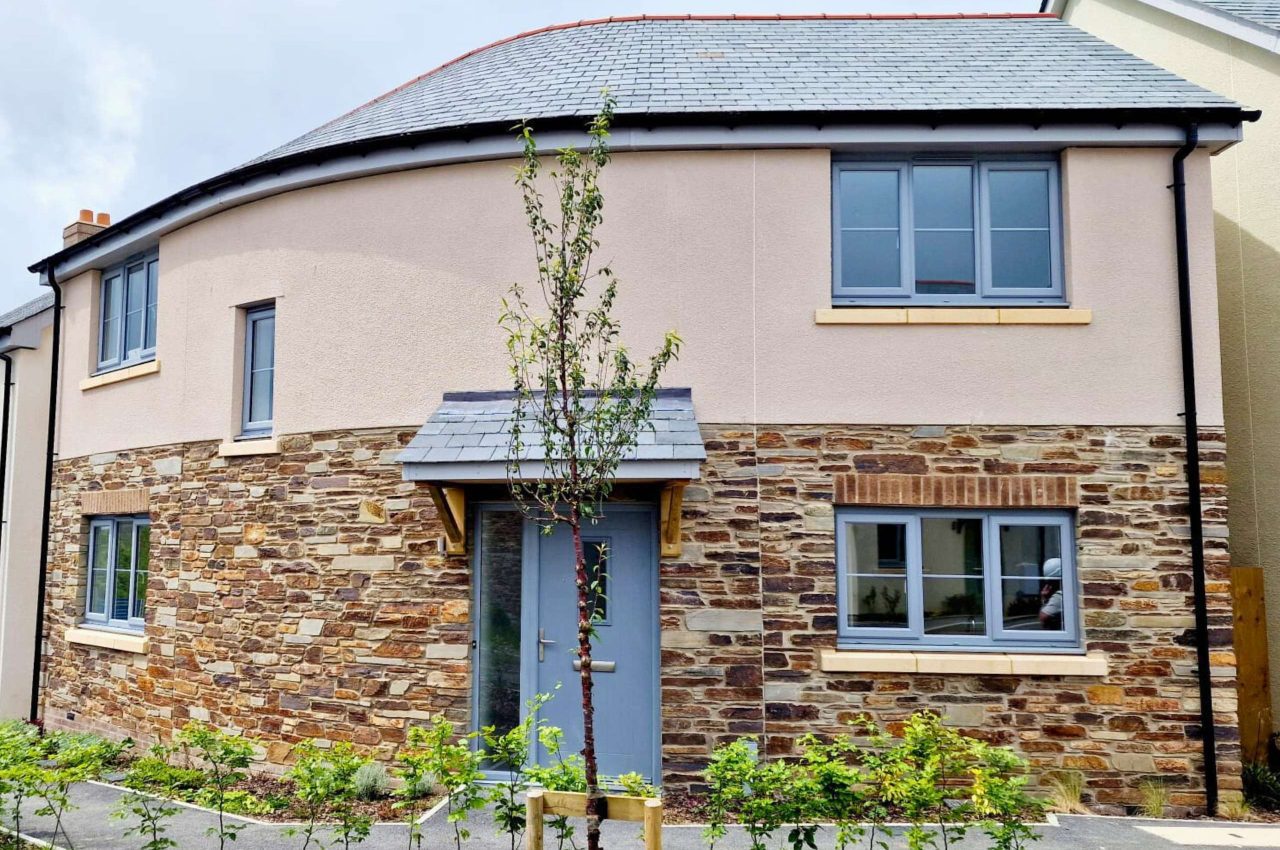 Photograph of a house finished with render and stone. To the front is pathway and planting.