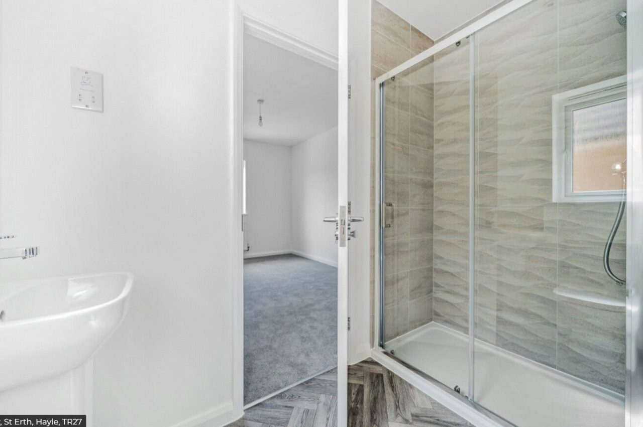 Image of an ensuite showing the sink and shower cubicle, with grey tiles.