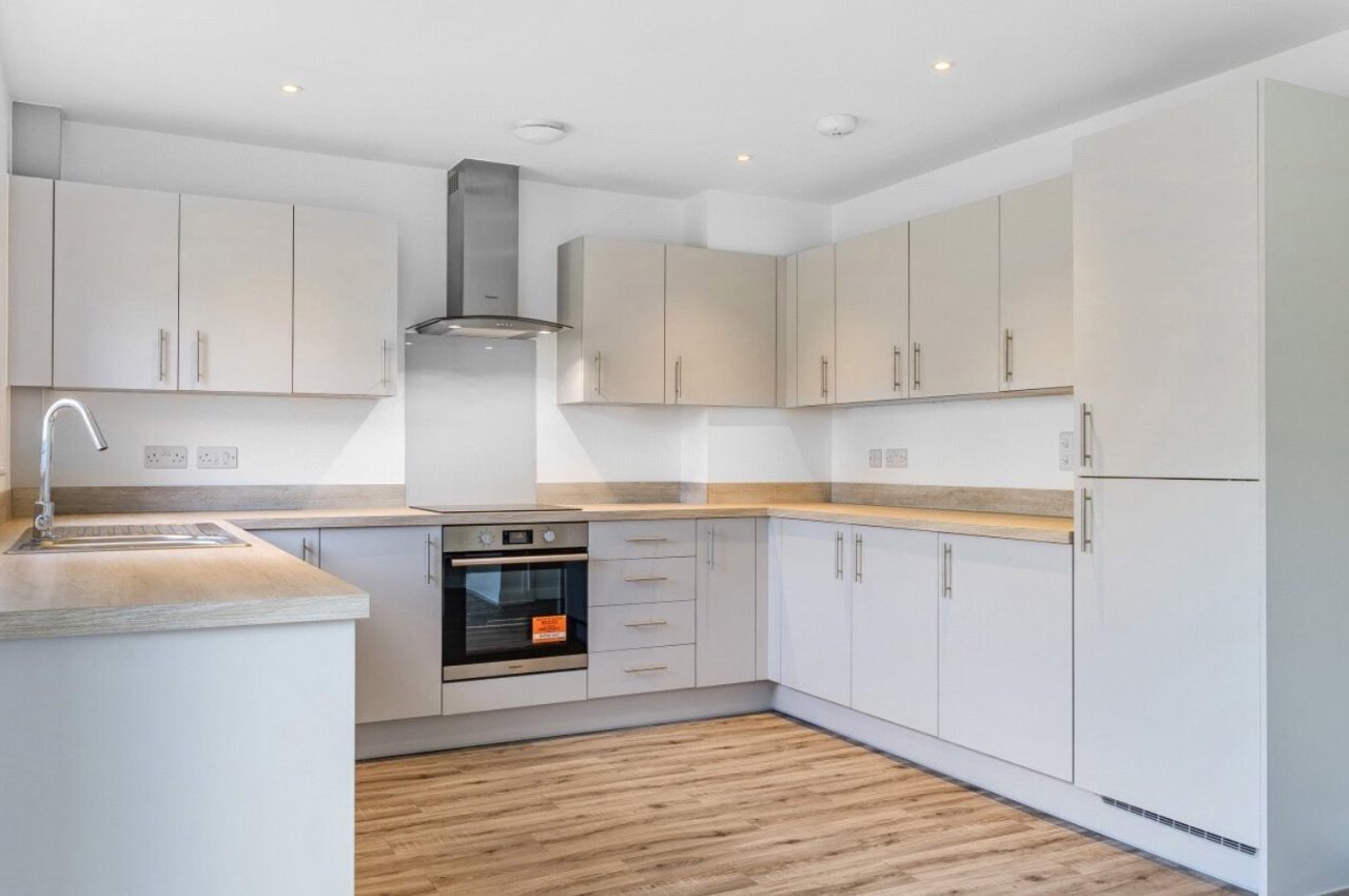 Image of a U-shaped kitchen with grey cabinet doors and oak worktop, complemented with oak-style flooring.